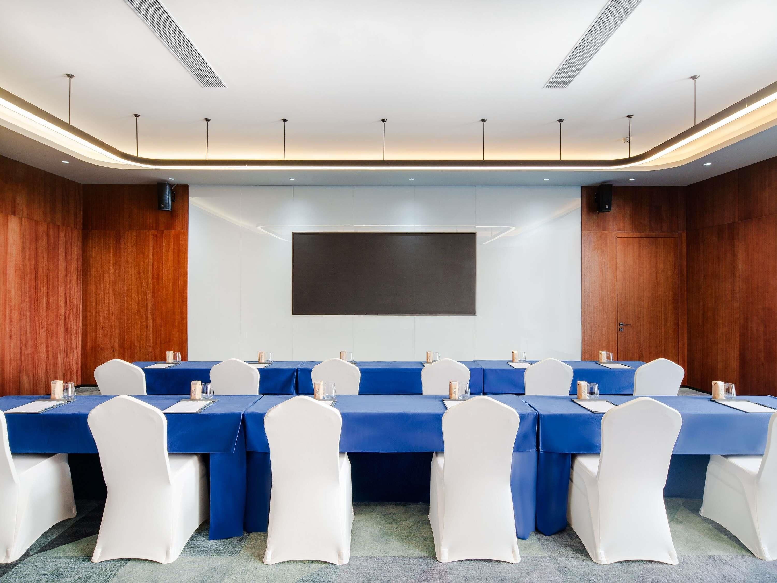 A conference room with a long table, white chairs, and a large screen.