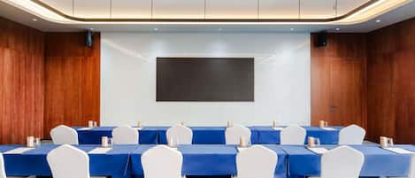 A conference room with a long table, white chairs, and a large screen.