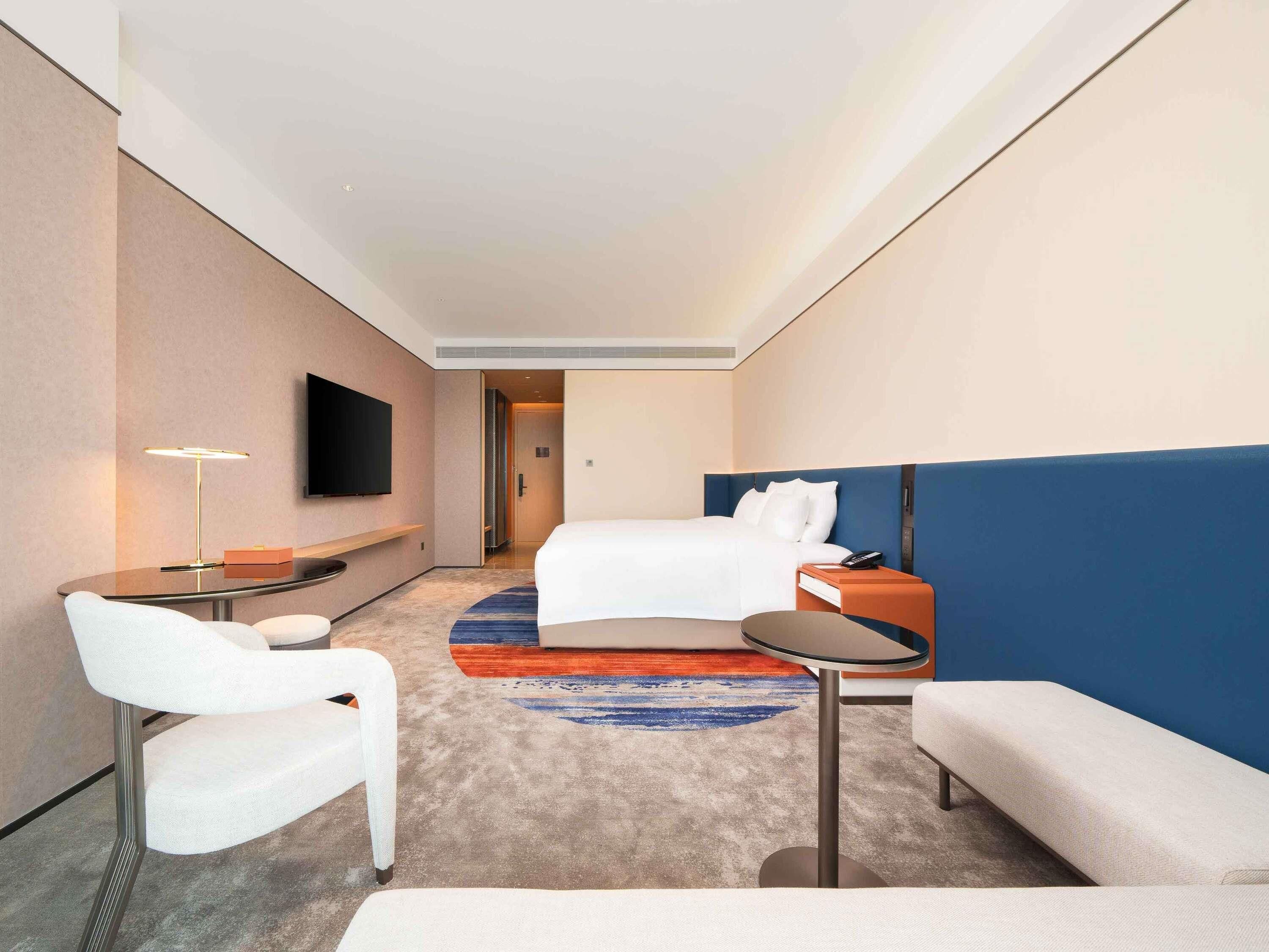 Una habitación de hotel con cama, escritorio, silla, televisor y una pequeña mesa.