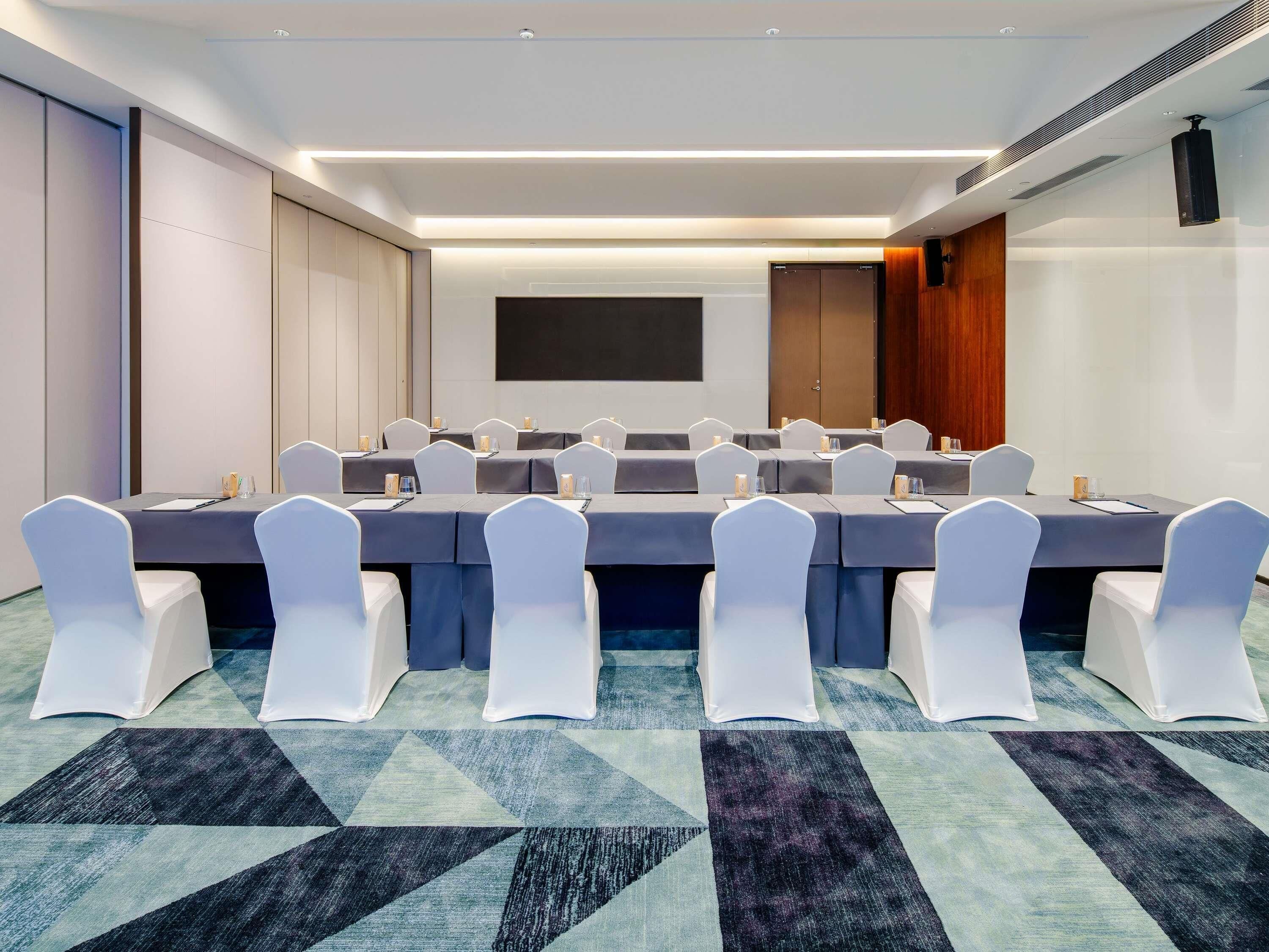 A conference room with a long table, white chairs, and a projector screen.