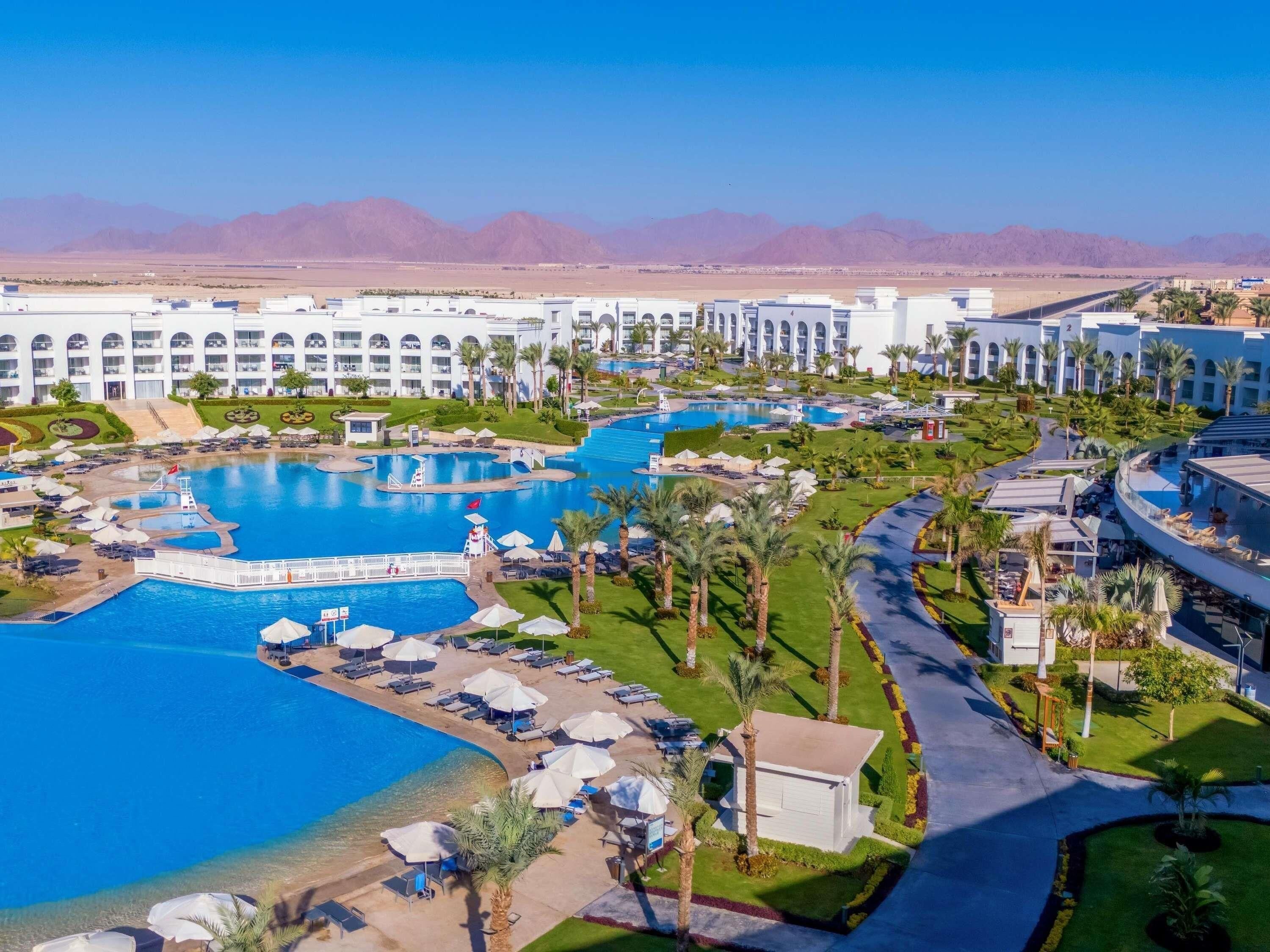 A resort with multiple swimming pools, palm trees, and a large building with arched windows.