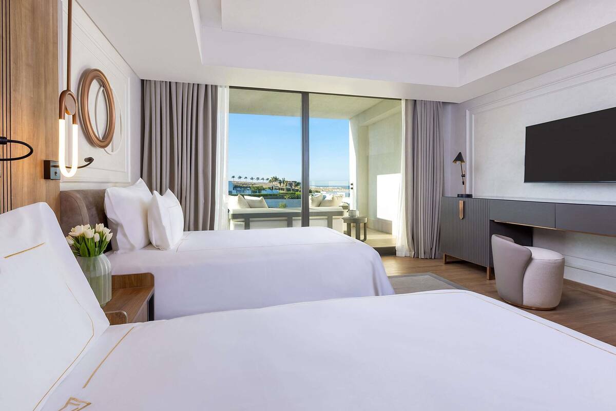 A hotel room with two beds, a TV, a balcony with a view, and a dining area.