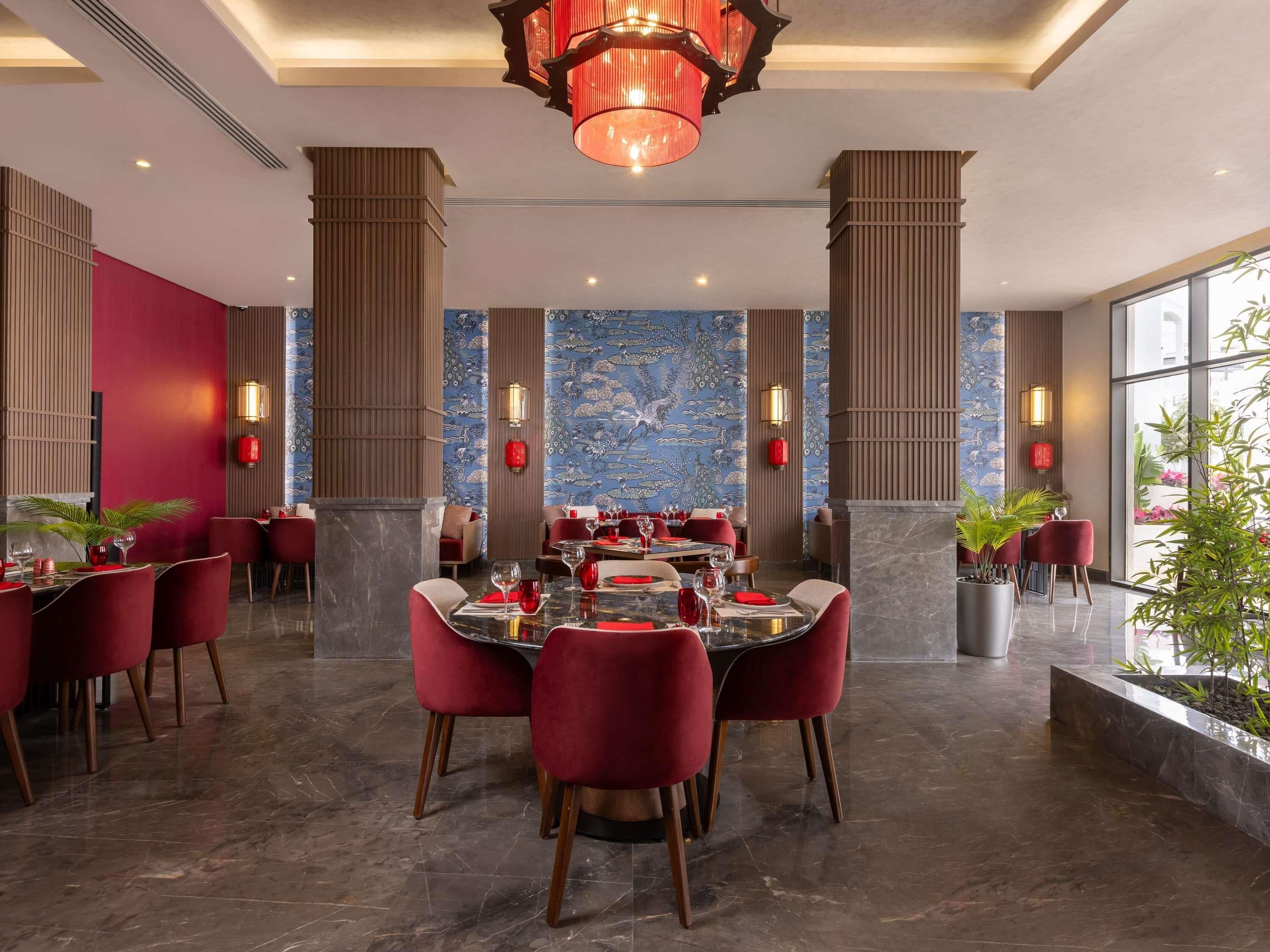 Uma área de jantar moderna com uma mesa central, cadeiras vermelhas e painéis decorativos na parede.