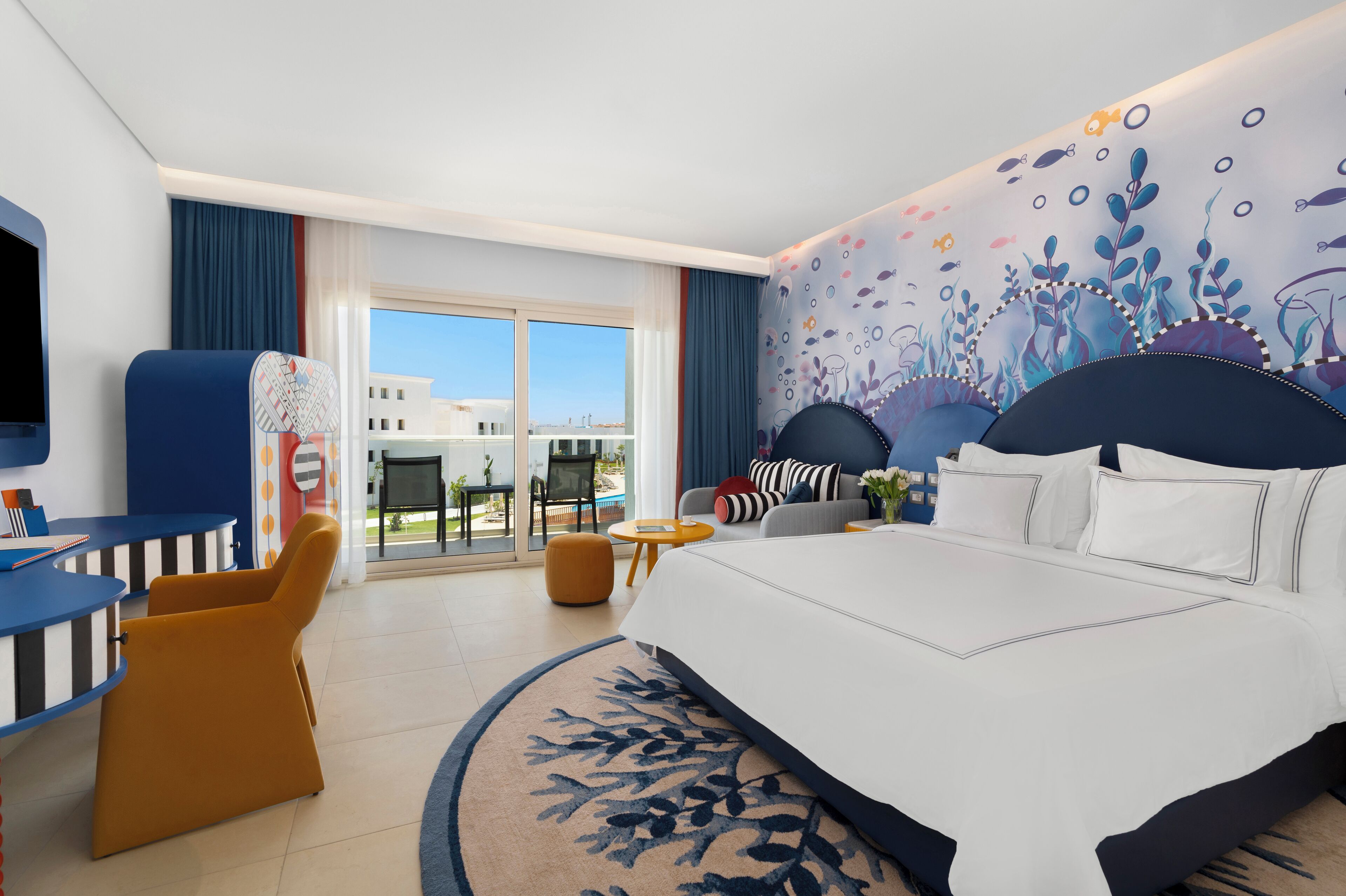 A hotel room with a large bed, a desk, a chair, and a view of the outdoors.