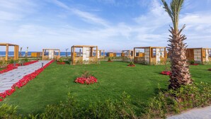 A series of wooden cabins with a clear view of the ocean, arranged in a row with a pathway lined with red flowers. - Rixos Radamis Sharm El Sheikh (Sharm El Sheikh)