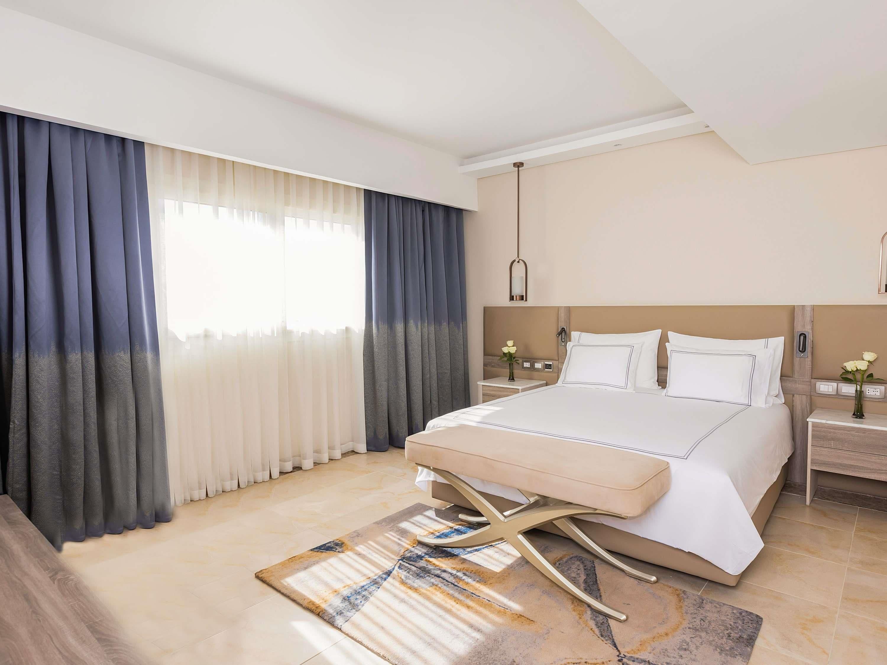 Habitación de hotel con cama, mesitas de noche, lámpara y ventana con cortinas.