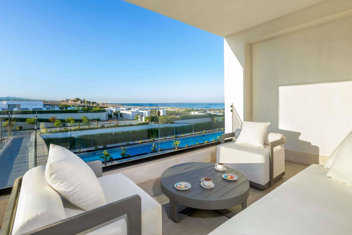Un balcón con piscina, mobiliario blanco y vista al mar.