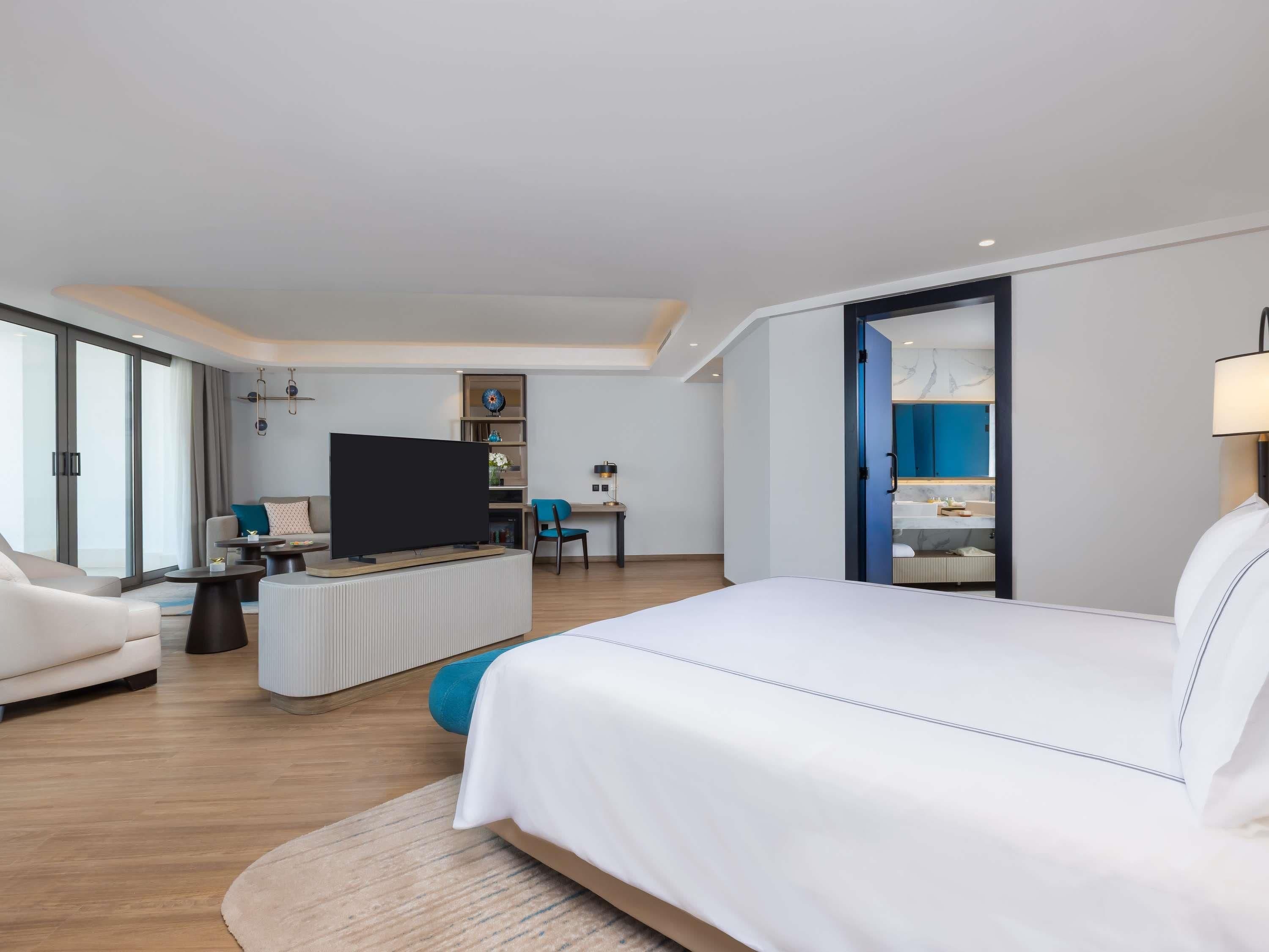 A modern hotel room with a large bed, a flat-screen TV, a desk, and a seating area.