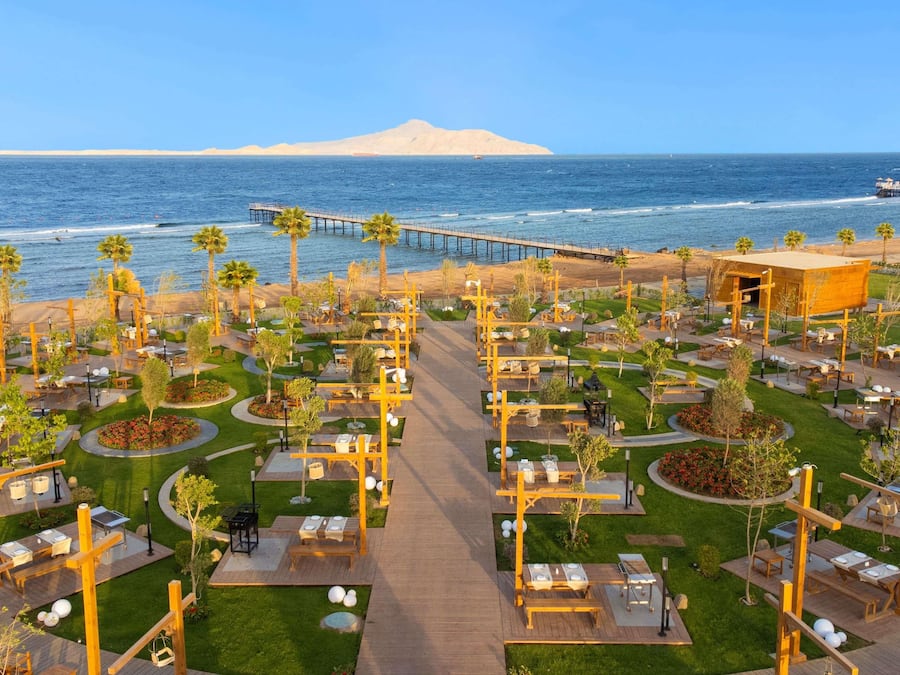 A coastal resort with outdoor dining areas, palm trees, and a view of the ocean.