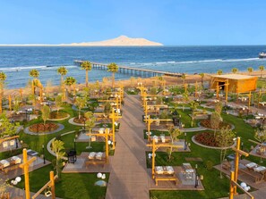 A coastal resort with outdoor dining areas, palm trees, and a view of the ocean. - Rixos Radamis Sharm El Sheikh (Sharm El Sheikh)