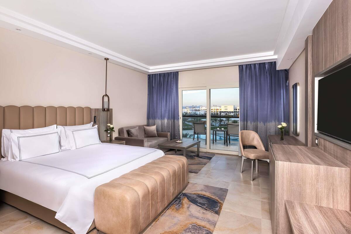 A hotel room with a large bed, a sofa, a desk, and a TV.