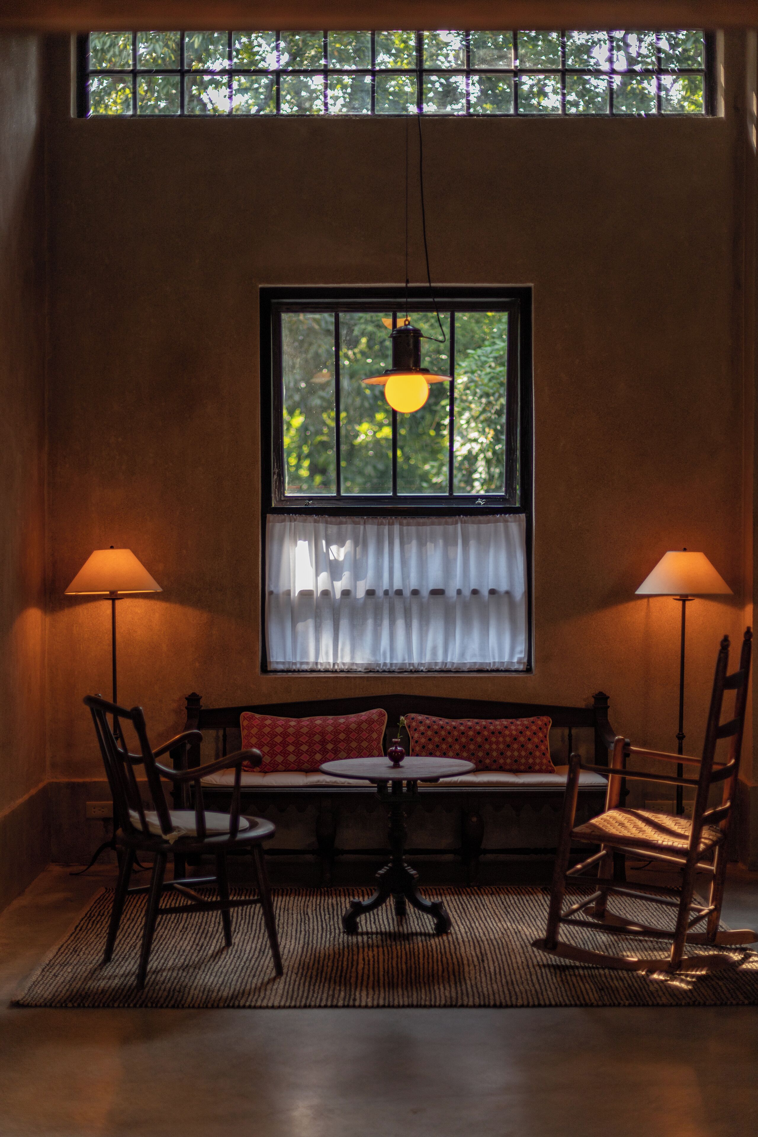 A room with a bench, two chairs, a table, and a window with curtains.