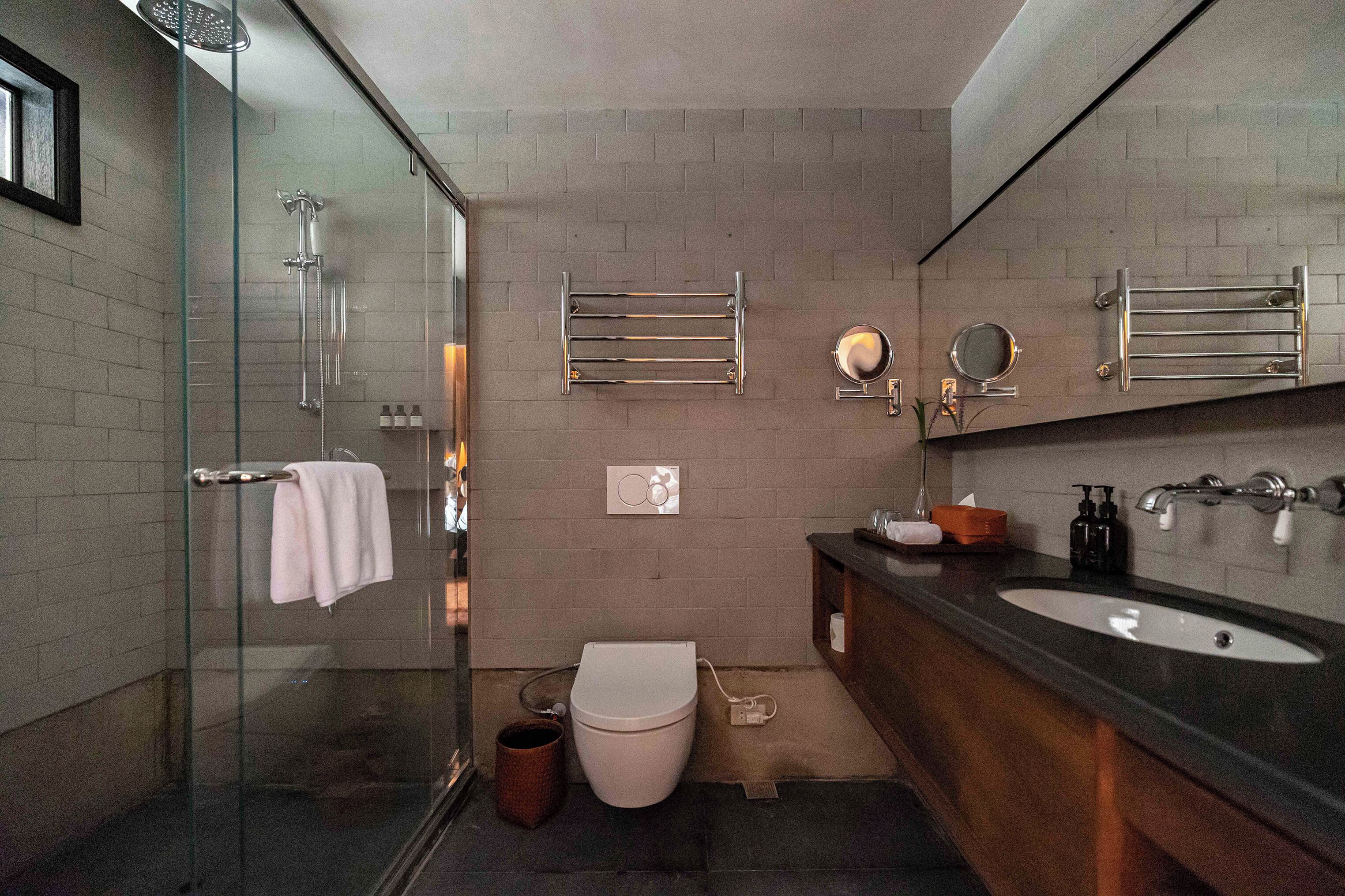 A modern bathroom with a glass shower enclosure, a white toilet, a sink with a dark countertop, and a mirror above the sink.