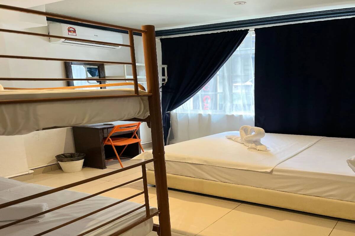 Een slaapkamer met stapelbed, bureau, stoel, klein tafeltje en raam met gordijnen.