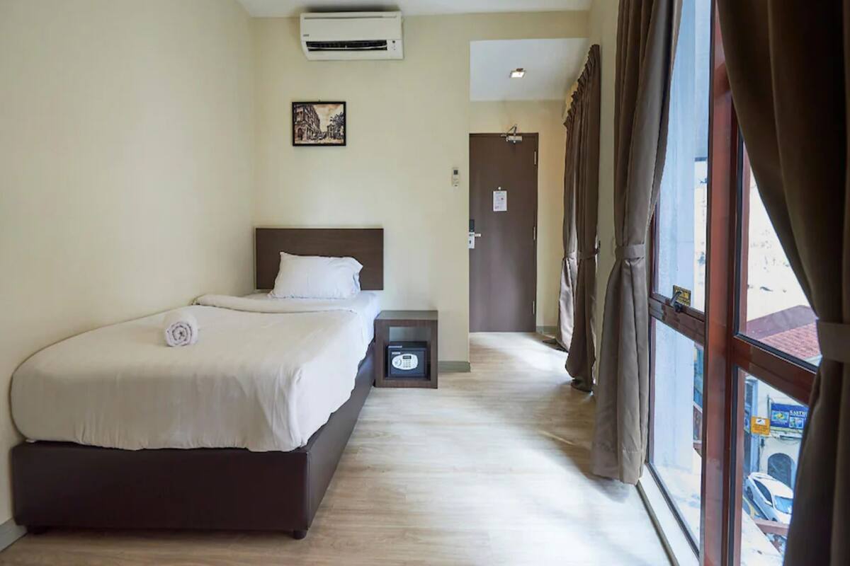 Een hotelkamer met een bed, een airconditioner, een nachtkastje, een deur en een raam met gordijnen.