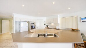 Een moderne keuken met een centraal eiland, roestvrijstalen apparatuur en uitzicht op de woonkamer.