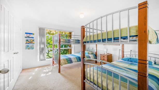 Een kamer met stapelbedden, een raam met zonwering en een deur.