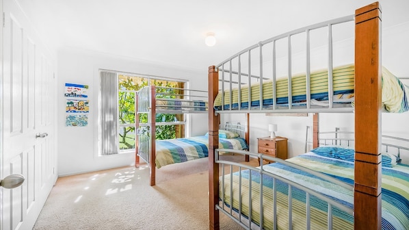 A room with bunk beds, a window with blinds, and a door.