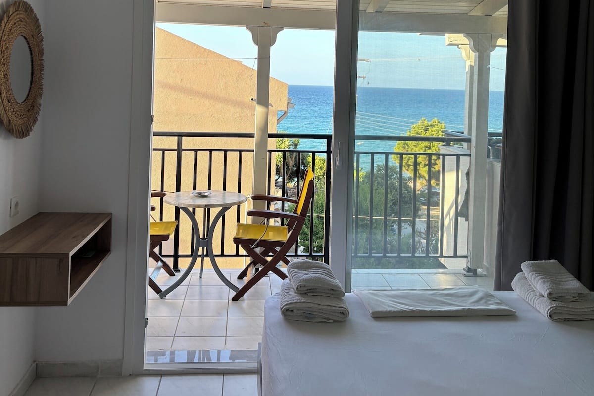 A hotel room with a balcony, a bed, a small table, and a chair.