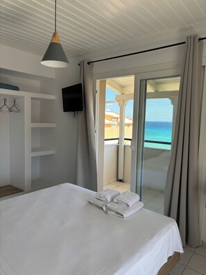 A bedroom with a bed, a TV, a ceiling fan, and a view of the ocean. - Vaso Alykanas Studios (Zakynthos)