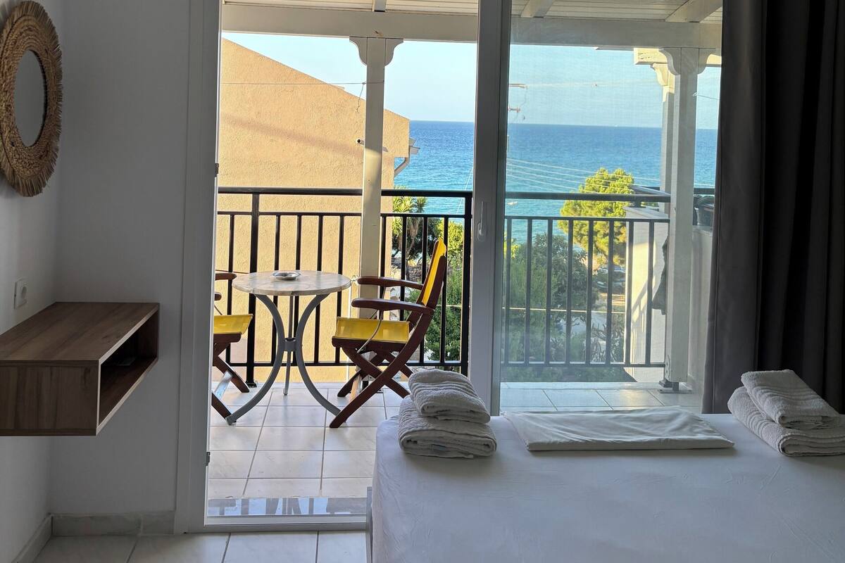 Una habitación de hotel con balcón, cama, una pequeña mesa y una silla.