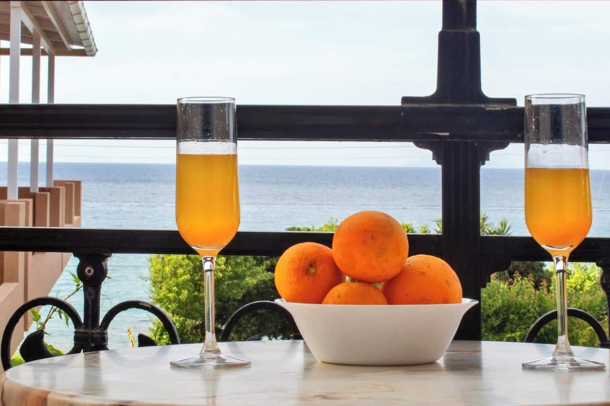 Una mesa con dos vasos de jugo de naranja y un bol de naranjas, con vista al mar.