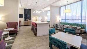 A modern hotel lobby with a central island, seating areas, and a large window with curtains. - La Quinta Inn And Suites By Wyndham Columbus Ms (Columbus)