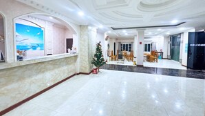 Un lobby espacioso con suelo de mármol, una recepción, un árbol de Navidad y un comedor con sillas y mesas.