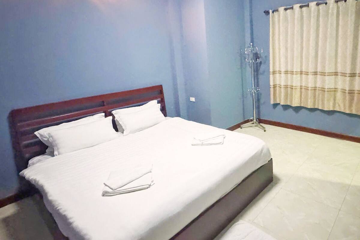 A neatly made bed with white linens and pillows, a wooden headboard, and a bedside table.