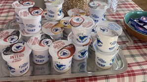 Et bord med forskelligt mad, herunder yoghurtglas, en kande og en kurv med brød.