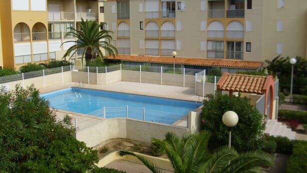 A swimming pool surrounded by a fence, with a building in the background. - Location Narbonne Plage (Villefranche-de-Rouergue (12))