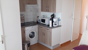 A compact kitchen with a washing machine, microwave, and coffee maker. - Location Narbonne Plage (Villefranche-de-Rouergue (12))