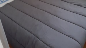 A small, single-bed room with a wooden headboard, a grey mattress, and a blue patterned pillow. - Location Narbonne Plage (Villefranche-de-Rouergue (12))