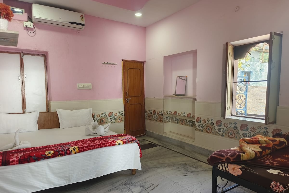 A bedroom with a bed, a wooden door, an air conditioning unit, a window, and a decorative wall panel.