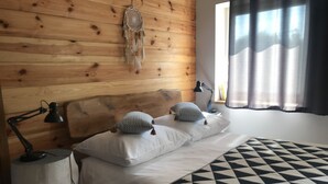 Una cama bien hecha con un edredón de estampado geométrico, dos almohadas y un atrapasueños en la cabecera.
