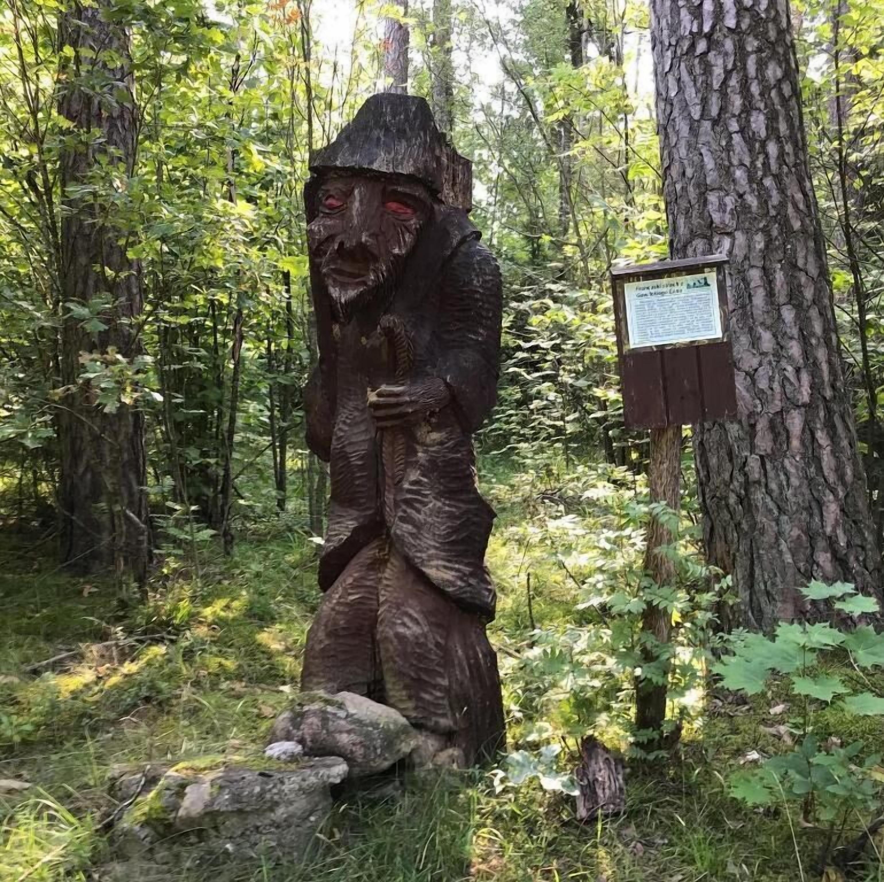 Eine Holzskulptur einer Gestalt in einer Waldlandschaft.