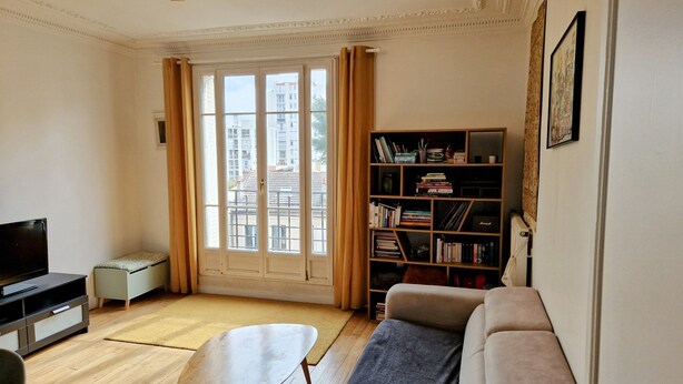 A living room with a sofa, a coffee table, a TV, a bookshelf, and a window with curtains. - Appartement Familial Proche de la Gare de Clamart (Clamart)