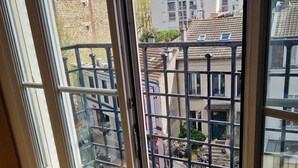 A room with a large window overlooking a courtyard with a green lawn and a metal fence. - Appartement Familial Proche de la Gare de Clamart (Clamart)