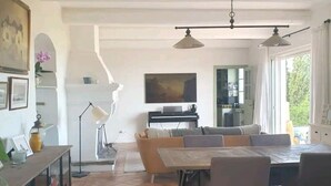 A spacious living area with a dining table and chairs, a television, and a kitchen area in the background. - Maison de Charme Avec vue Imprenable à 5 Minutes de L'ile Rousse (Monticello)