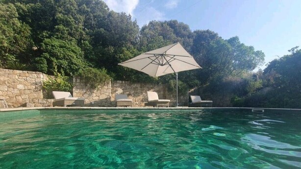 A clear pool with lounge chairs and an umbrella, surrounded by stone walls and greenery. - Maison de Charme Avec vue Imprenable à 5 Minutes de L'ile Rousse (Monticello)