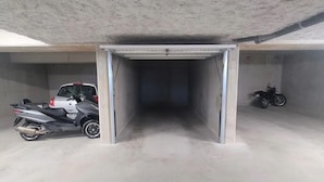 Un parcheggio sotterraneo con soffitto e pareti in cemento, una moto e un'auto parcheggiate all'interno.