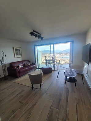 Een ruime woonkamer met een groot raam, een bank, een salontafel en een televisie.