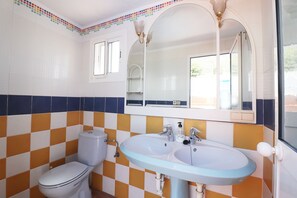 A bathroom with a white toilet, two sinks, and a mirror above the sinks.