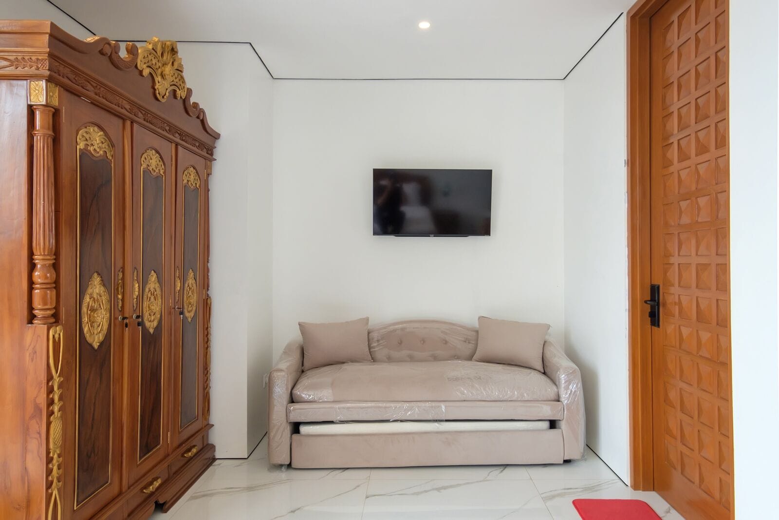 A room with a sofa, a television mounted on the wall, and a wooden cabinet.