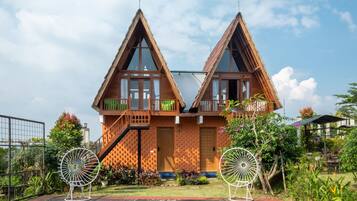 Een symmetrisch houten huis met twee balkons, een centrale deur en een kleine tuin met twee decoratieve windvaan-spinners.