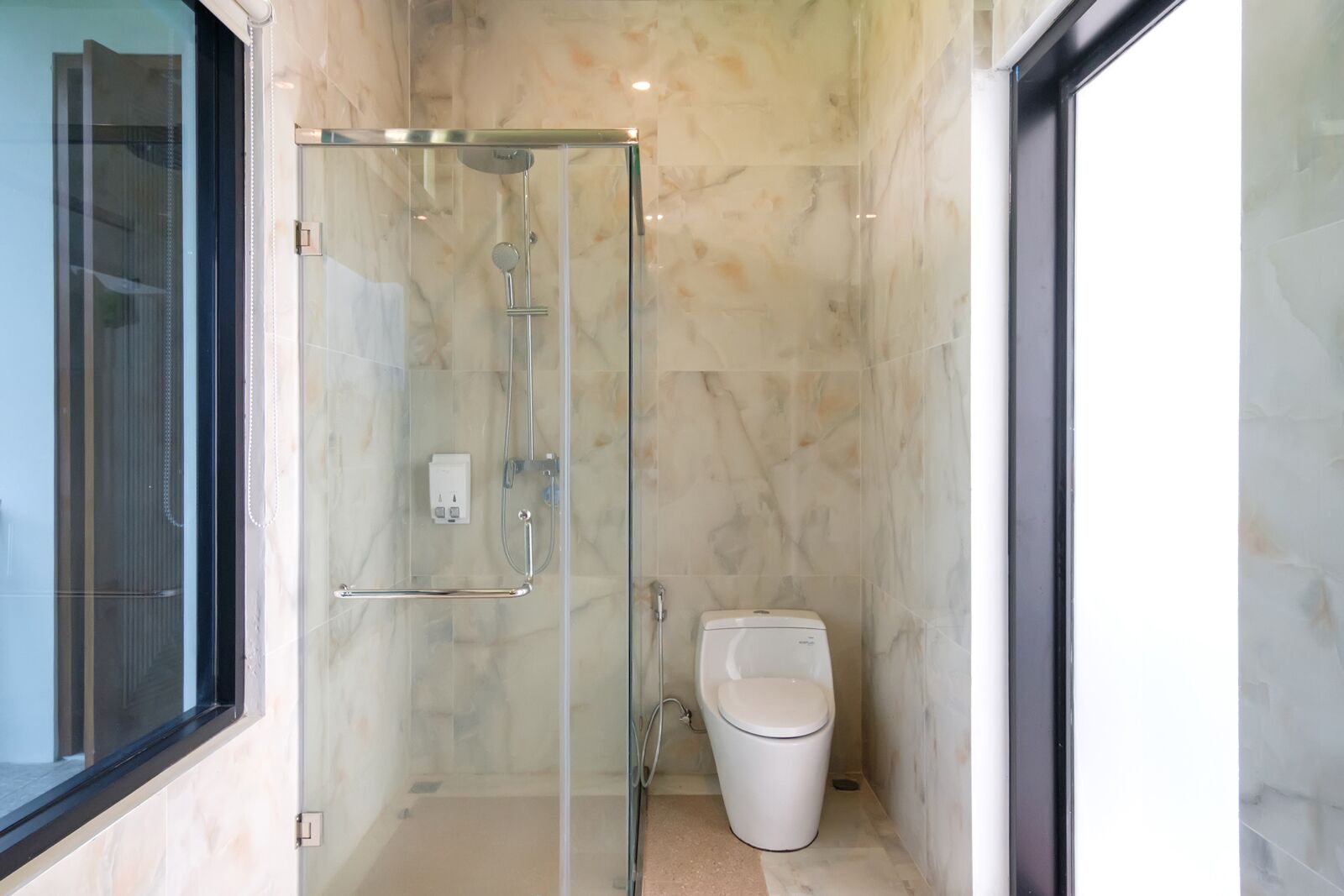 A modern bathroom with a glass-enclosed shower, a toilet, and a marble-tiled wall.