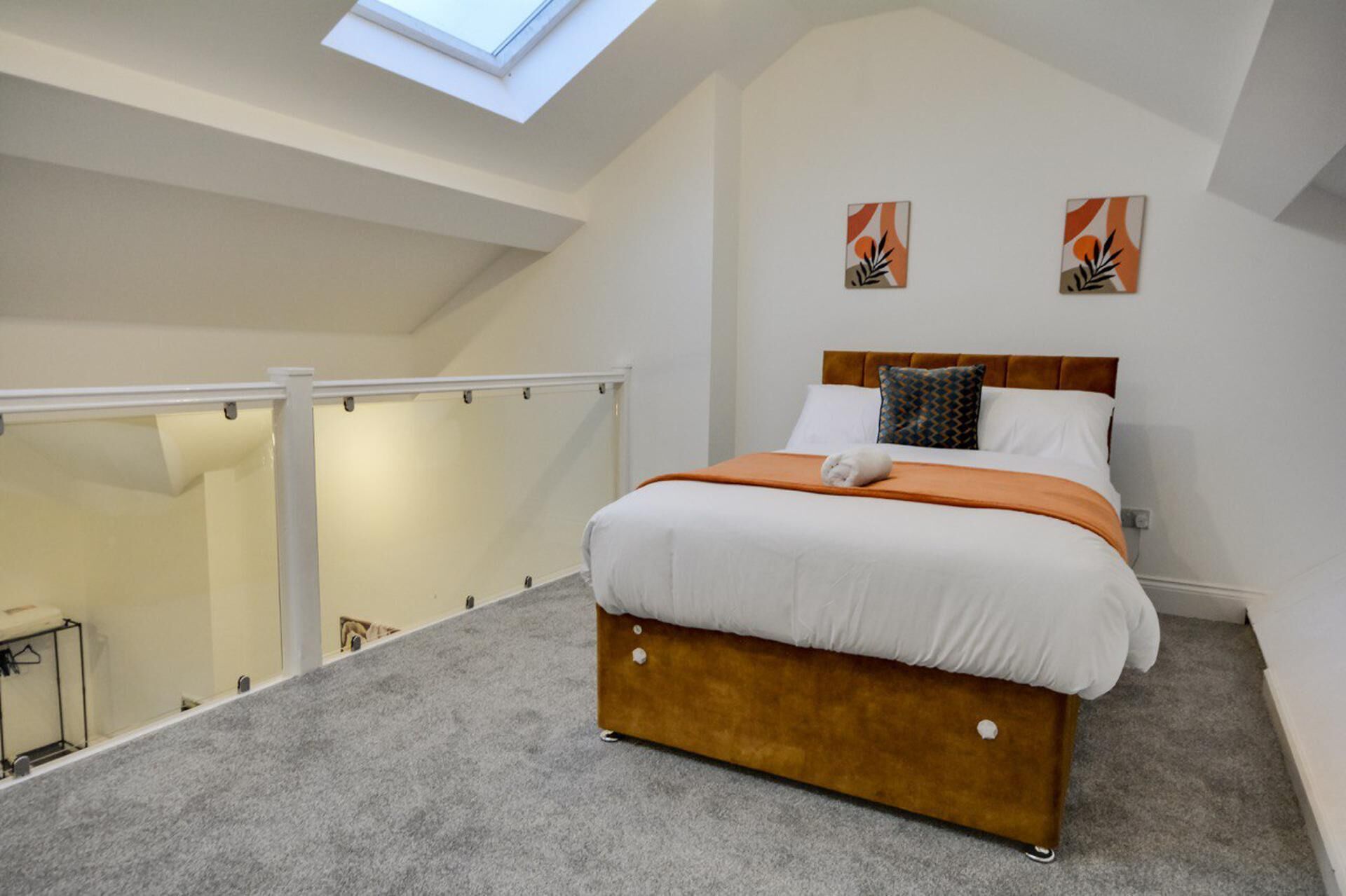 A bedroom with a bed, a skylight, and two wall art pieces.