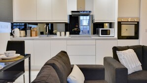 Una cocina moderna con armarios blancos, microondas y horno. Hay una zona de comedor con mesa y sillas.