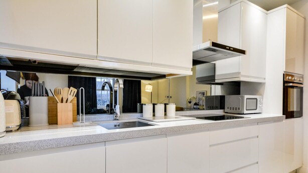 Una cocina moderna con armarios blancos, una campana extractora de acero inoxidable, microondas integrado y un lavamanos doble.
