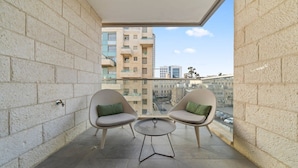 Ein Balkon mit zwei Stühlen und einem kleinen Tisch, Blick auf Gebäude und einen klaren Himmel.